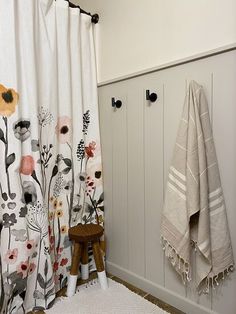 a white bathroom with floral shower curtain and wooden stool