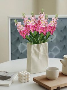 pink flowers are in a white vase on a table next to a book and cup