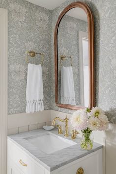 a white sink sitting under a mirror next to a wooden framed mirror on top of a wall