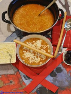 two bowls of soup and bread on a red place mat with utensils next to it