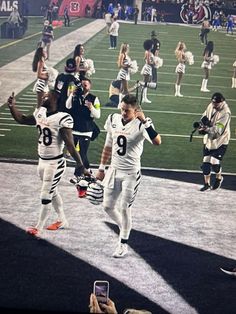 two football players are walking off the field with their arms in the air as people take pictures