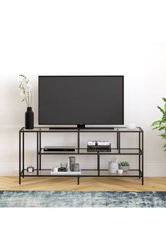 a flat screen tv sitting on top of a metal shelf next to a potted plant