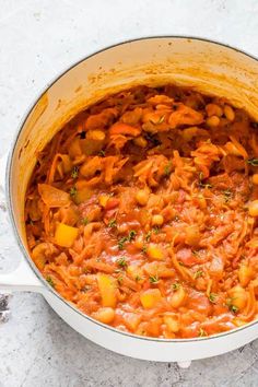 a pot filled with pasta and vegetables on top of a white countertop next to a wooden spoon