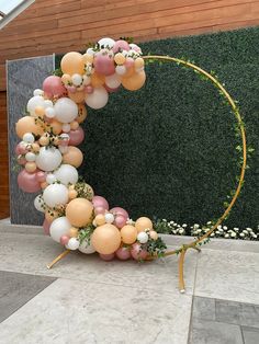 an arch made out of balloons and greenery in front of a building with a green wall behind it