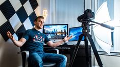 a man sitting in front of a computer on top of a desk next to a camera