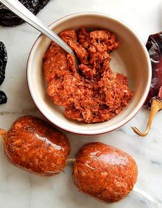 a bowl filled with meat next to two other food items on a marble counter top