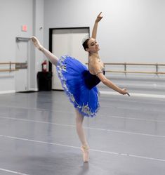 a young ballerina in a blue tutu and leotard doing a ballet move