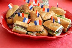 a plate full of sandwiches with toothpicks sticking out of them on red table cloth