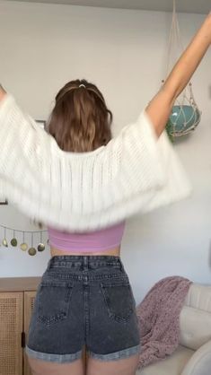 a woman with her arms in the air, standing next to a white couch and shelves