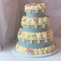 a three tiered blue and white cake with flowers on the top is sitting on a table