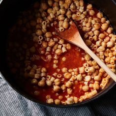 a wooden spoon in a pot filled with some kind of pasta and meat sauce on top of a blue cloth