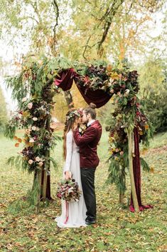 a bride and groom kissing under an arch decorated with flowers, greenery and foliage