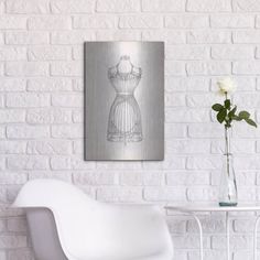 a white chair sitting in front of a wall with a vase and flowers on it