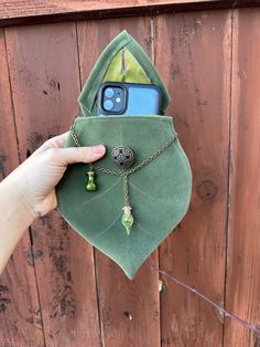 someone is holding their cell phone in a green pouch on the side of a wooden fence