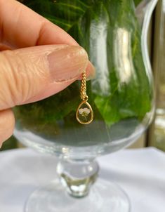 a person holding a tiny gold necklace in front of a vase filled with green plants