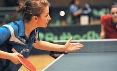 a woman is playing ping pong on a court with other people in the background