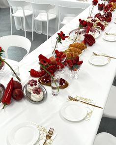 a long table with plates, silverware and red flowers on it is set for a formal function