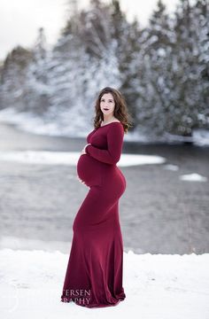 a pregnant woman standing in the snow with her hands on her hips, wearing a long red dress