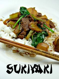 a white plate topped with meat and vegetables next to chopsticks on top of rice