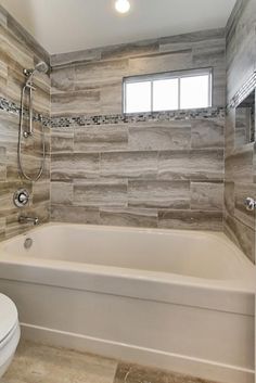 a white toilet sitting under a window next to a bath tub in a room with tile walls