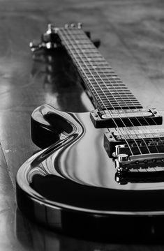 a black and white photo of a guitar laying on the floor with it's frets