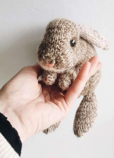 a hand holding a small stuffed animal in it's right hand, against a white wall