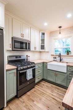 an empty kitchen with green cabinets and white walls, wood flooring and stainless steel appliances