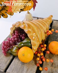 a wooden table topped with oranges and grapes next to a carved cornucopia