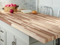 a large wooden cutting board sitting on top of a kitchen counter next to a basket of apples