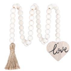 the white beaded necklace with love charm and tassel is shown next to a wooden heart