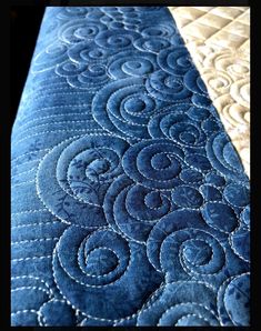 a close up view of a blue quilted bed cover with swirls on it