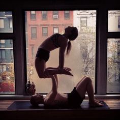 two women are doing yoga in front of a window with city buildings and trees outside