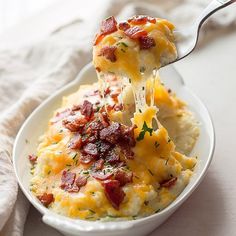 a white bowl filled with mashed potatoes covered in bacon and cheese, being held by a fork