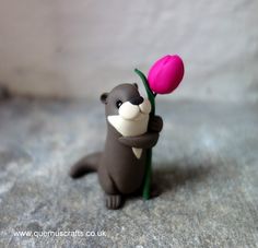 a toy otter holding a pink flower in its mouth on top of a gray surface