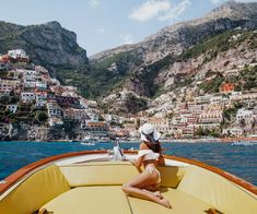 a woman sitting on the back of a boat in front of a mountain town and ocean