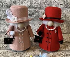 two small dolls are dressed up in red and pink outfits, one is wearing a hat