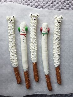 four snowman pretzels are lined up on a sheet of wax paper and decorated with icing