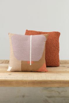 two pillows sitting on top of a wooden table next to an orange and pink pillow