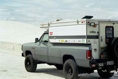 a truck with a camper attached to the back parked on a sandy area in front of sand dunes