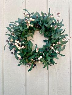 a wreath with white berries and green leaves hanging on the side of a wooden wall