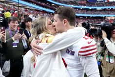 a man and woman kissing in front of a crowd at a sporting event with cameras around them