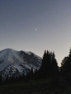 the moon is setting over a mountain with trees in front of it and an airplane flying overhead