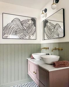 two sinks in a bathroom with mirrors above them and paintings on the wall behind them