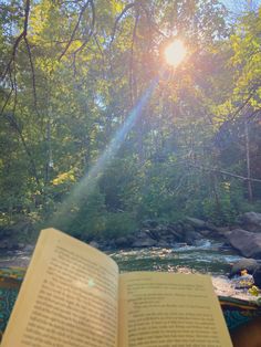 an open book sitting on top of a wooden table next to a river and forest