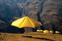 yellow umbrellas are set up on the side of a mountain with mountains in the background