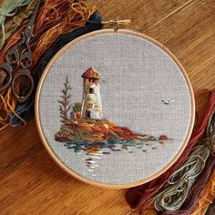 a cross stitch project with scissors and thread on the table next to it is an embroidered lighthouse