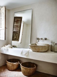 two baskets sit on the counter in front of a mirror and sink with an open shuttered window