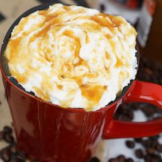 a red cup filled with whipped cream on top of coffee beans and caramel syrup