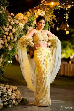 a woman in a yellow sari is standing under an arch with flowers on it