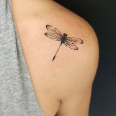 a small dragonfly tattoo on the back of a woman's shoulder and arm